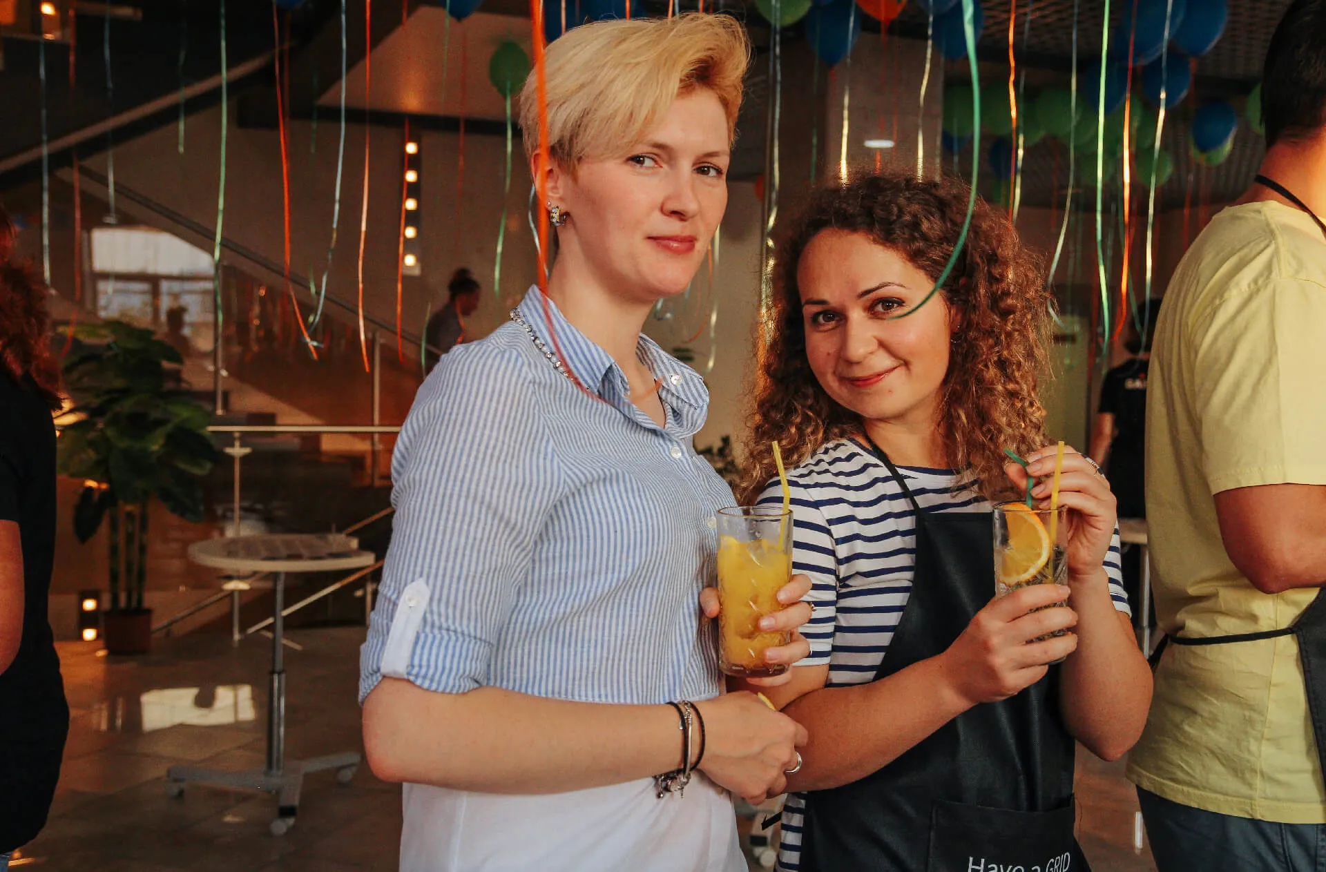 Two women smiling, holding drinks at a celebration