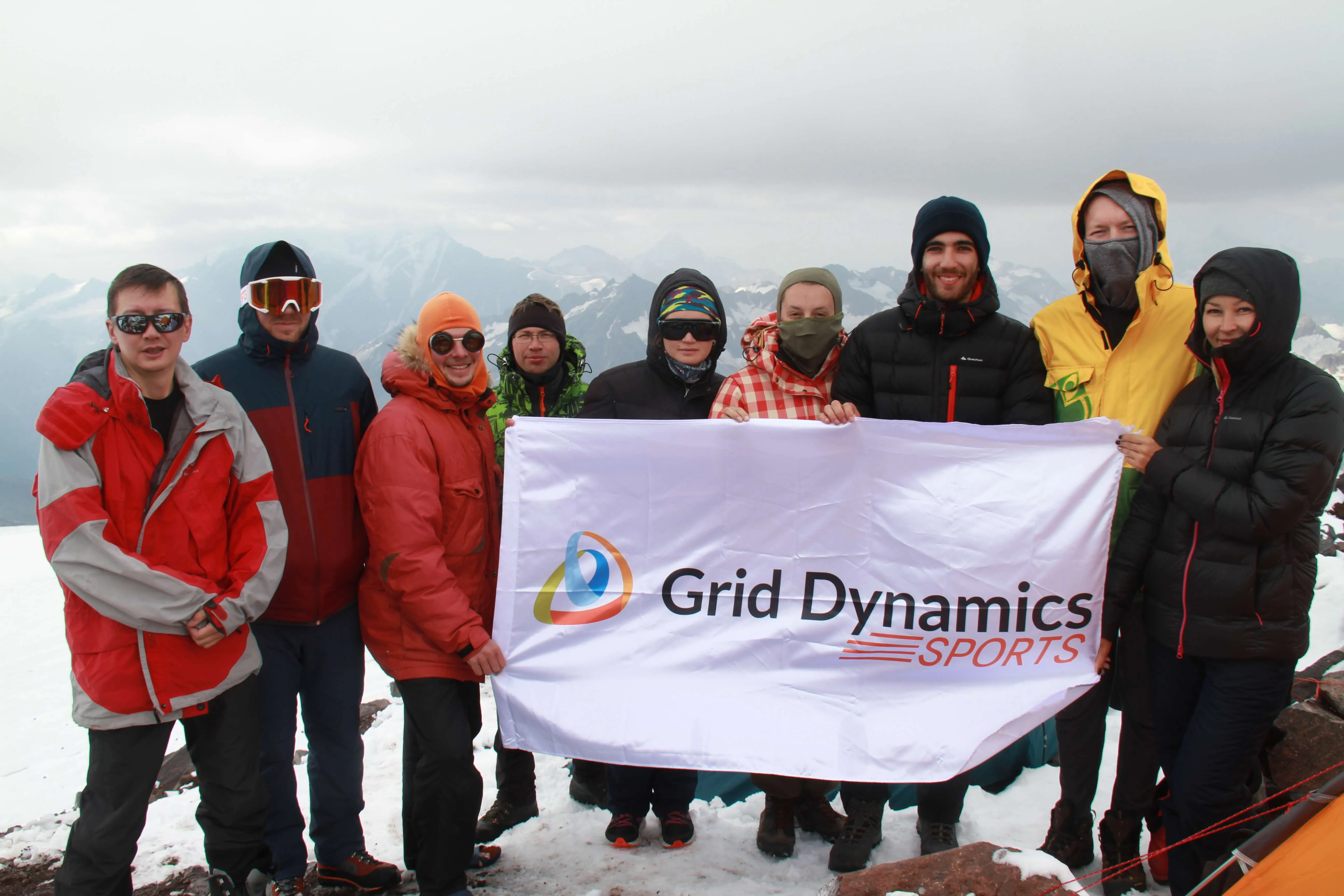 9 people holding Grid Dynamics flag on the top of the mountain